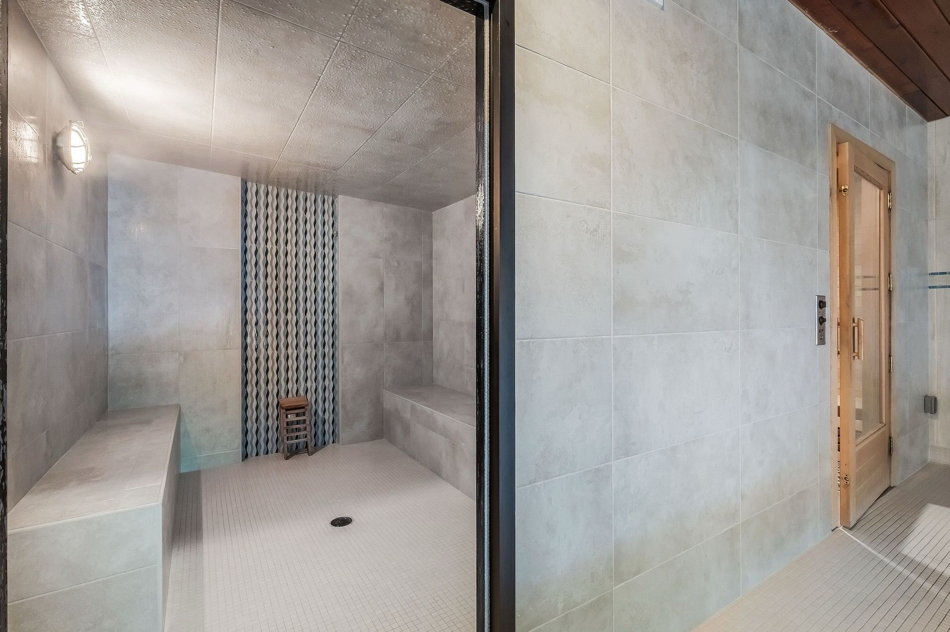 A modern bathroom with a shower, a bench, and a patterned wall.