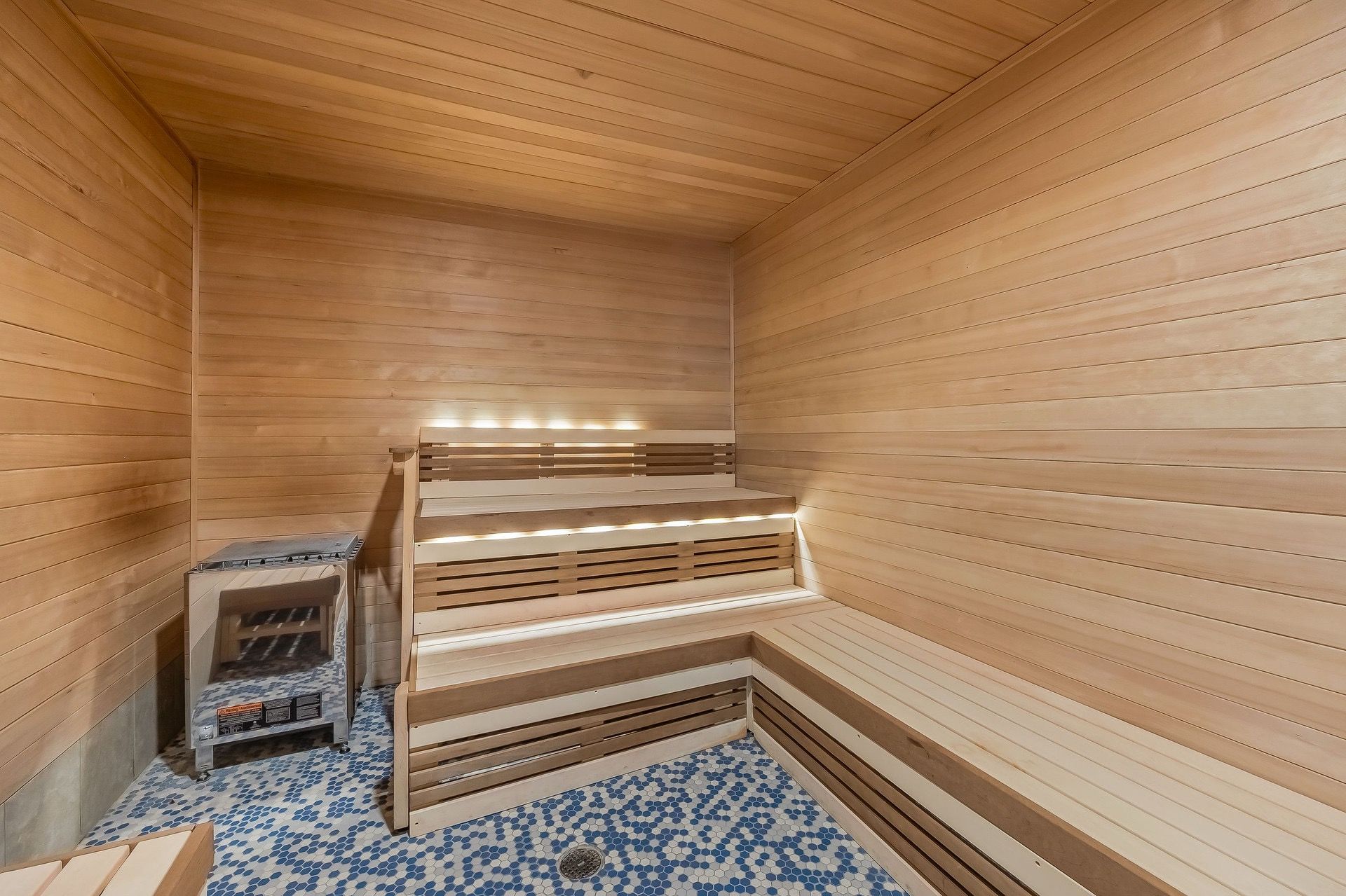 Una sauna con paredes y bancos de madera, piso de baldosas y un estante pequeño con objetos.