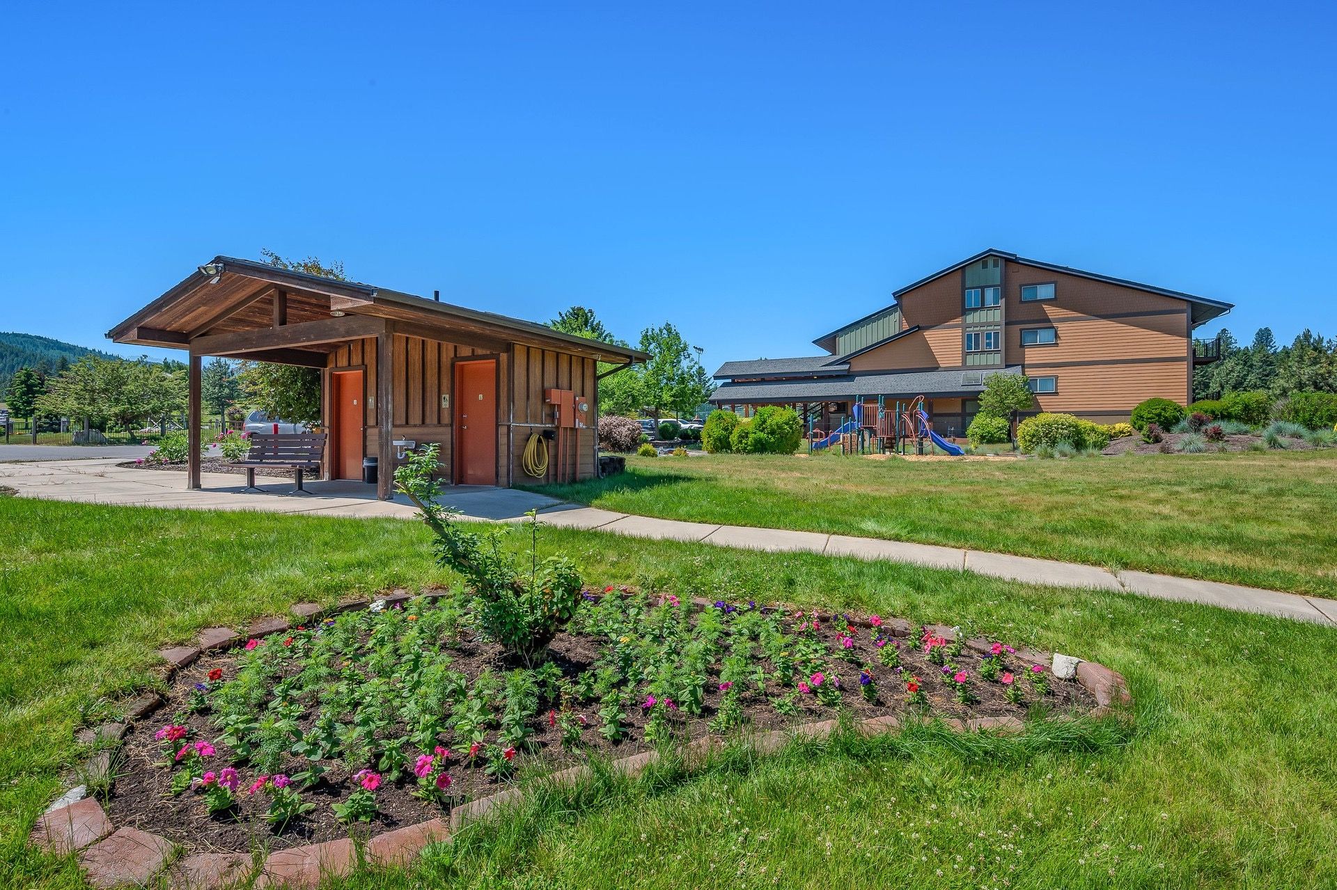 A building with a covered outdoor area, a playground, and a flower garden.