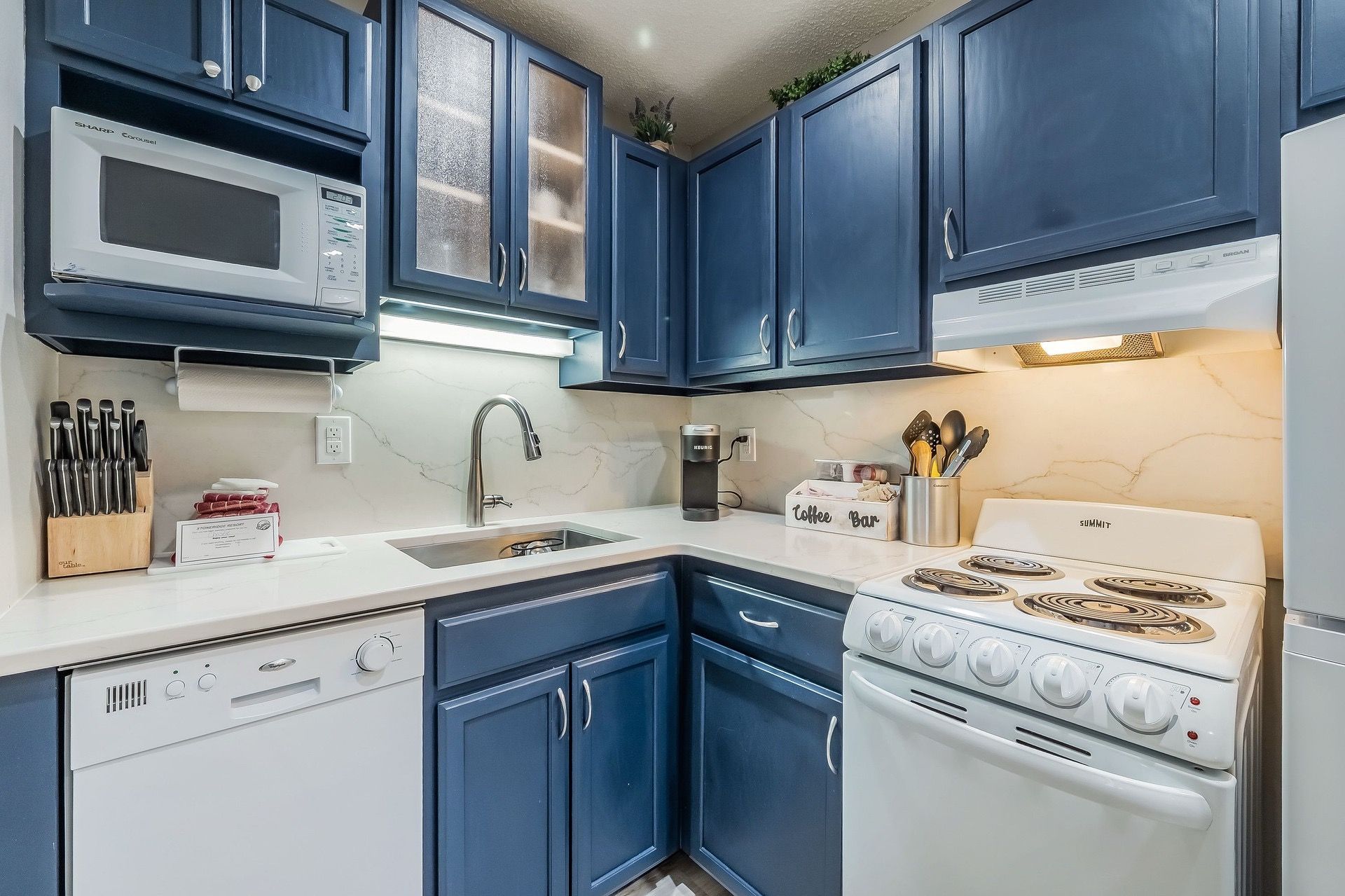 A kitchen with blue cabinets, a white microwave, a coffee maker, and a stove.
