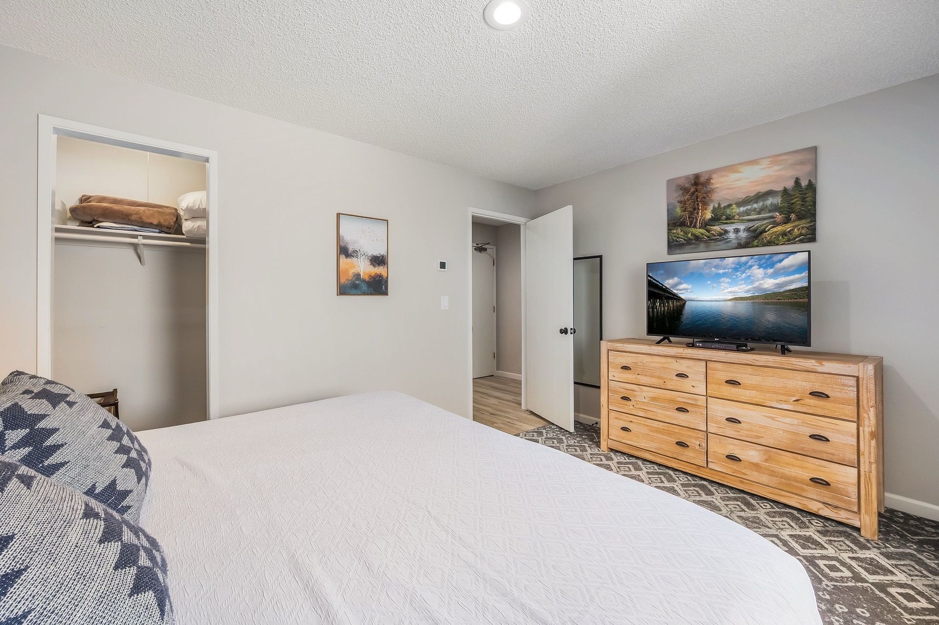 Un dormitorio con cama, cómoda, televisor y cuadros en la pared.