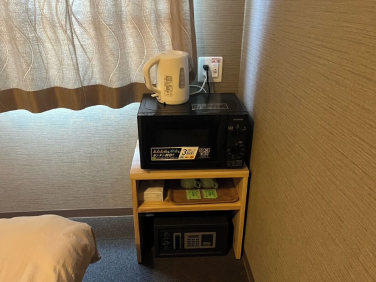 Un four à micro-ondes posé sur une étagère en bois, une bouilloire et un petit réfrigérateur dans une chambre d’hôtel.
