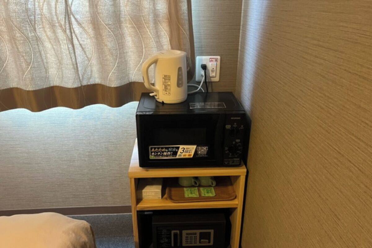 Een magnetron, waterkoker en kleine koelkast op een houten plank in een hotelkamer.