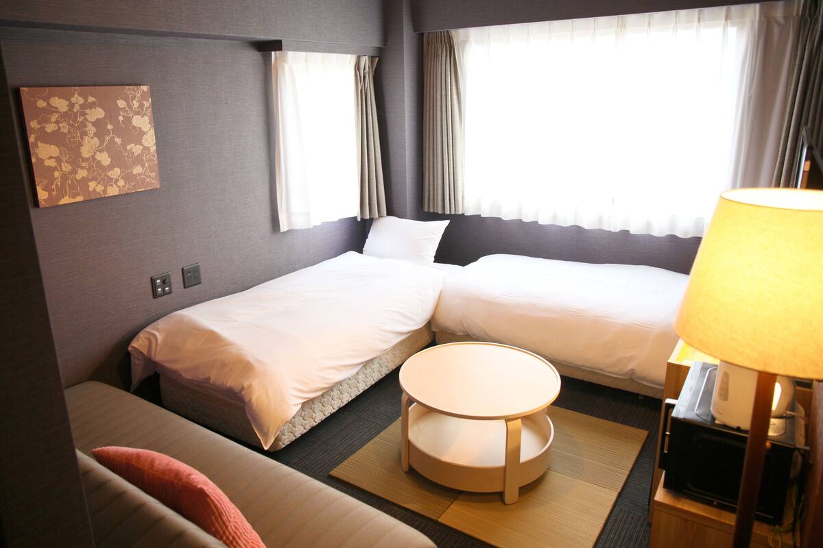 Een hotelkamer met twee bedden, een klein rond tafeltje, een bank en een lamp.