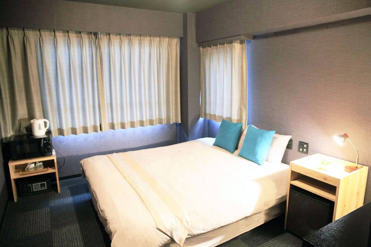 Een hotelkamer met een bed, nachtkastje met lamp, koffiezetapparaat en gordijnen.