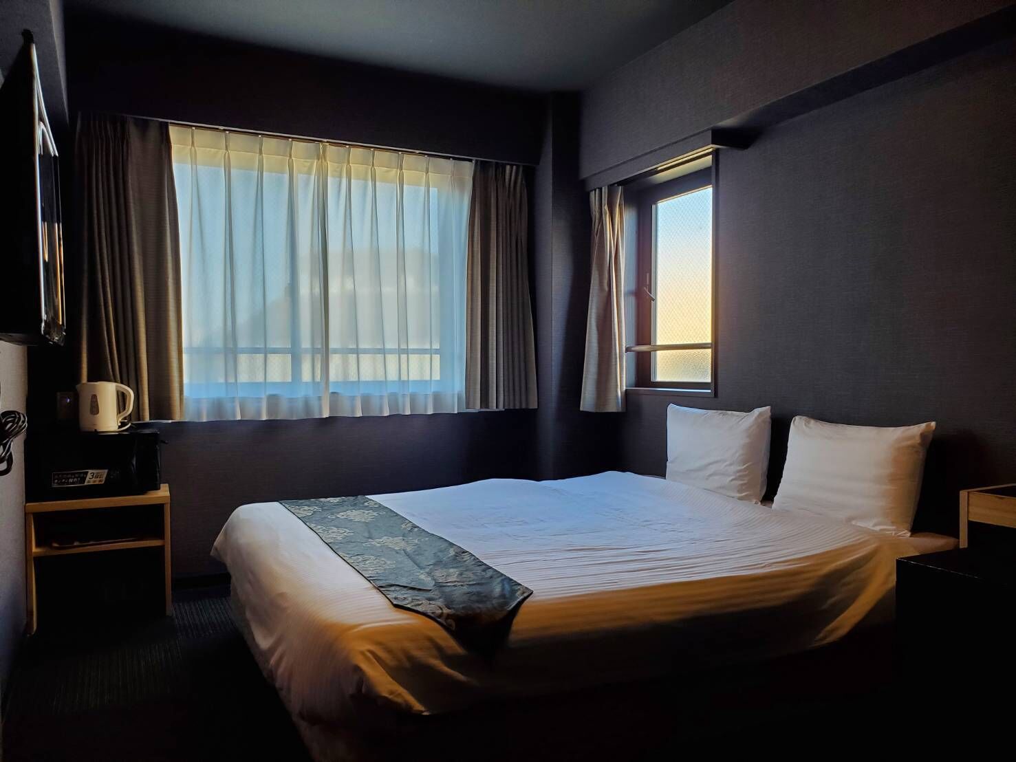 Une chambre d’hôtel avec un lit, une table de chevet, une machine à café et une fenêtre avec des rideaux.