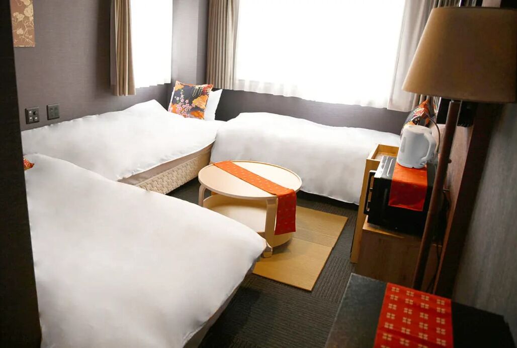 Une chambre d’hôtel avec deux lits, une petite table ronde, une lampe et une table d’appoint rouge.