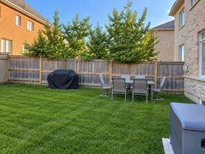 A backyard with a wooden fence, a covered grill, and a dining table with chairs.