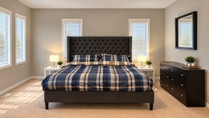 Une chambre à coucher avec un grand lit, deux tables de chevet, une commode et une fenêtre avec des stores.