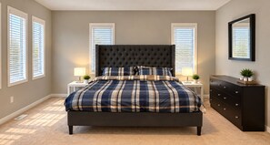 A bedroom with a large bed, two bedside tables, a dresser, and a window with blinds.