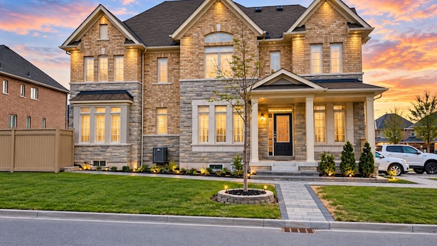 Une maison à deux étages avec une façade en pierre, un porche à l’avant et une pelouse bien entretenue.