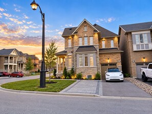 A residential street with houses, a street lamp, and parked cars.