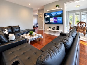 A modern living room with a black leather sofa, a coffee table with a magazine, and a flat-screen TV displaying streaming services.