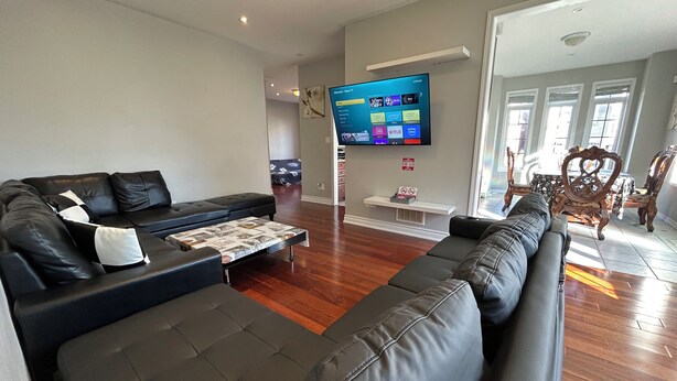 Una sala de estar moderna con un sofá grande de cuero negro, una mesa de centro y un televisor de pantalla plana montado en la pared.