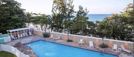 A swimming pool with lounge chairs and a view of the ocean.
