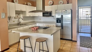 Una cucina moderna con mobili bianchi, un frigorifero in acciaio inossidabile, un forno a microonde e un'isola centrale con sgabelli.