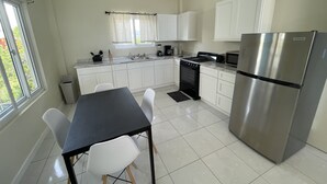 A modern kitchen with white cabinets, a stainless steel refrigerator, a stove, and a dining table with chairs. - Stylish 1 Bedroom Beach view (Belmont)