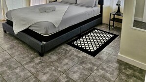 A modern bedroom with a grey bed, white bedding, and a black and white patterned rug. - Stylish 1 Bedroom Beach view (Belmont)