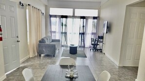 A spacious living room with a dark wooden table, white chairs, and a grey sofa. - Stylish 1 Bedroom Beach view (Belmont)