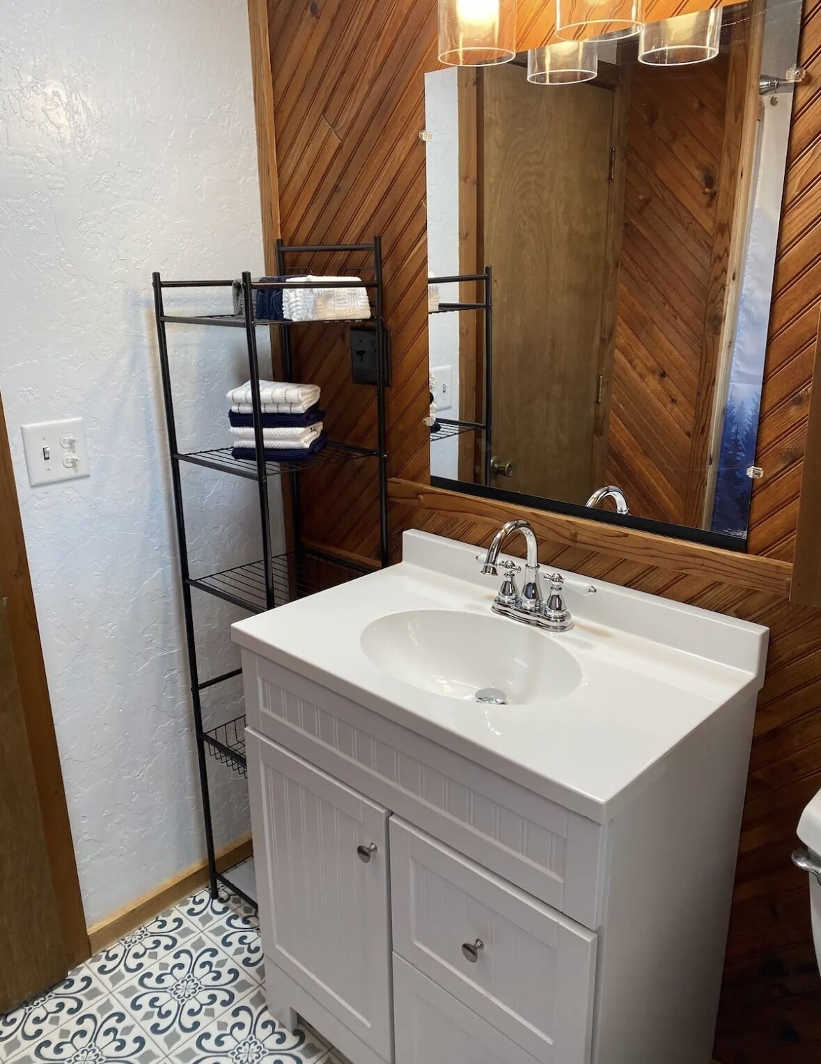 A bathroom with a white sink, wooden wall paneling, a mirror, and a towel rack with folded towels.