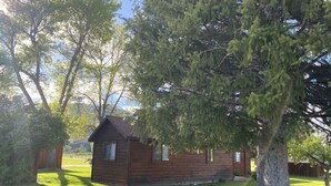 A small wooden cabin with a sloped roof, surrounded by a well-maintained lawn and tall trees. - Camas Creek Cabin (Hamilton)