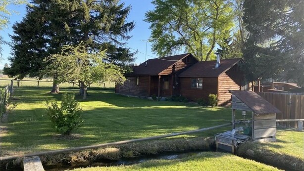 A wooden cabin with a sloped roof, surrounded by a well-maintained lawn and large trees. - Camas Creek Cabin (Hamilton)
