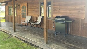 A wooden cabin with a porch, two folding chairs, and a grill. - Camas Creek Cabin (Hamilton)