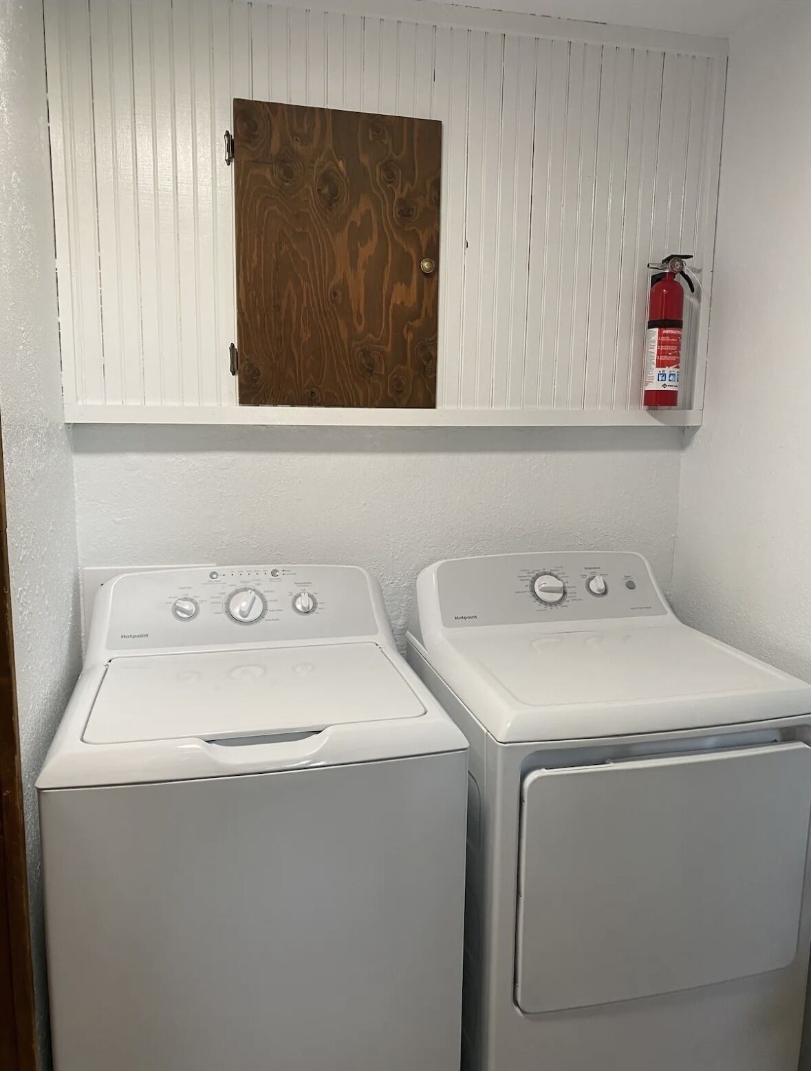 A laundry room with two white Hotpoint washers and a wooden door above.