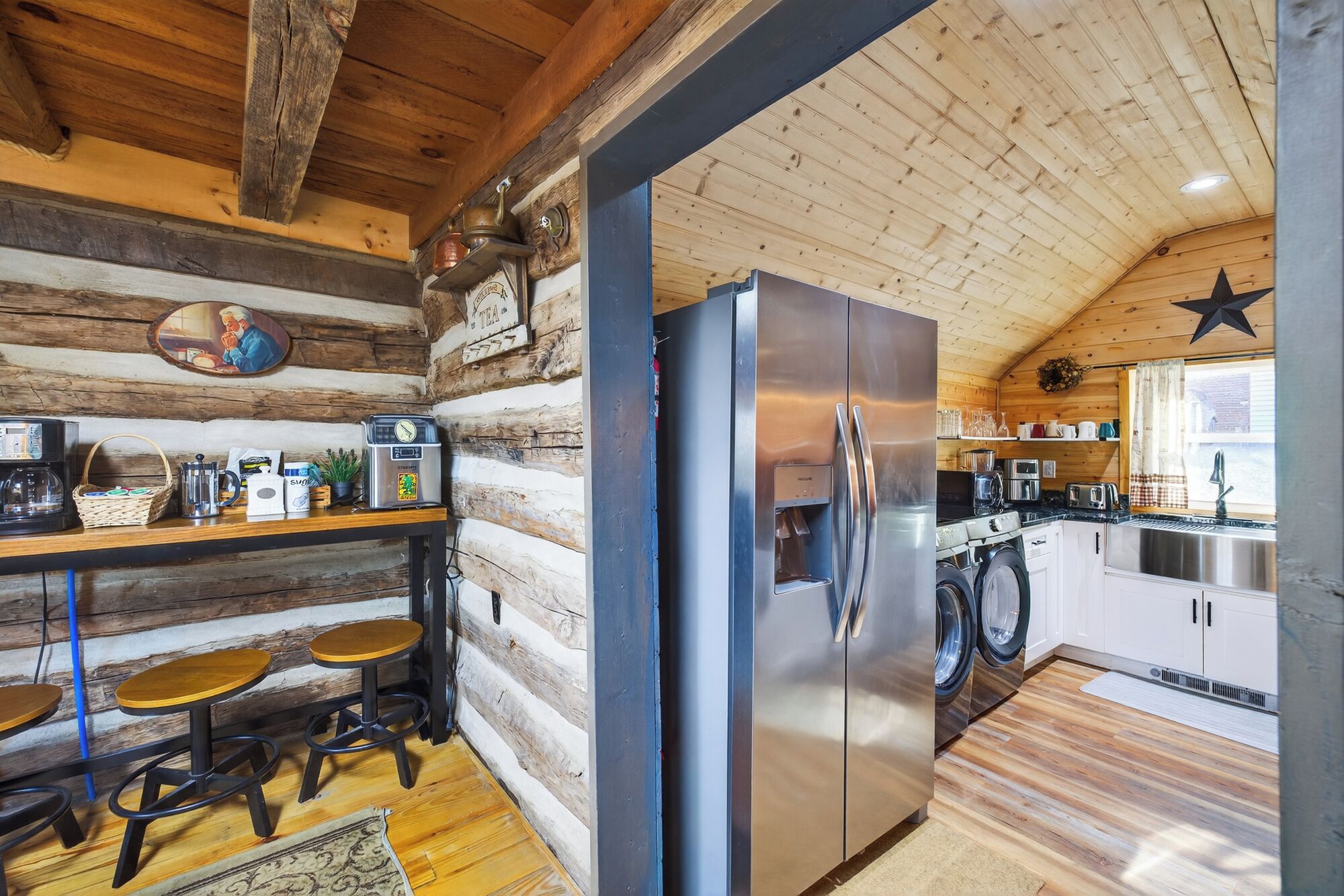Interior rústico de una cabaña con pared de madera, refrigerador de acero inoxidable, estación de café y lavadora.