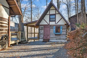 A log cabin with a steeply pitched roof, a wooden porch, and a gravel driveway.