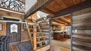 L’intérieur d’une cabane en rondins, avec un escalier en bois, un coin cuisine et un espace repas.