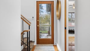 A wooden door with a glass panel, a staircase with wooden railings, and a view of a backyard with a patio and a tree. - Feet from Lake & Downtown, Pond View, Hot Tub,Pets (Northport)