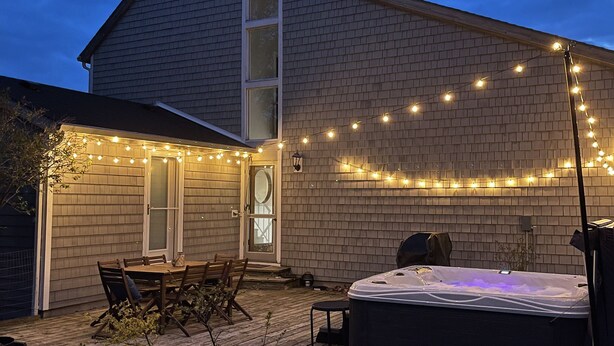 A two-story house with a brick exterior, a wooden deck, a hot tub, and string lights. - Feet from Lake & Downtown, Pond View, Hot Tub,Pets (Northport)