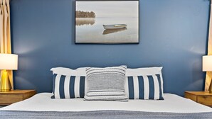 A bedroom with a large bed, two bedside tables with lamps, and a framed picture of a boat on water. - Feet from Lake & Downtown, Pond View, Hot Tub,Pets (Northport)