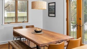 A dining area with a wooden table, leather bench, and a woven pendant light. - Feet from Lake & Downtown, Pond View, Hot Tub,Pets (Northport)
