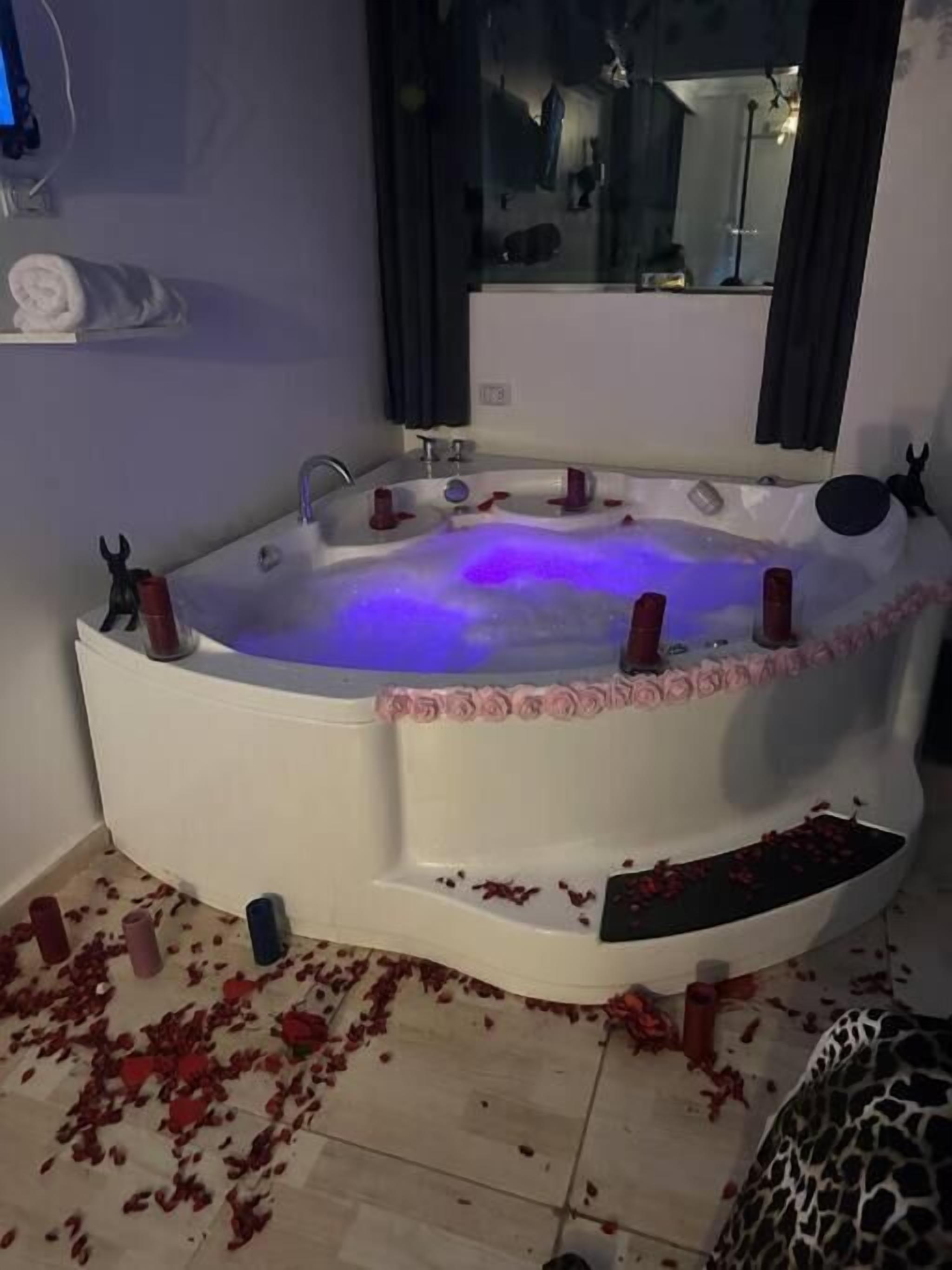 Eine große, weiße, freistehende Whirlwanne mit pinkfarbener Blütenbordüre und blauem Licht.