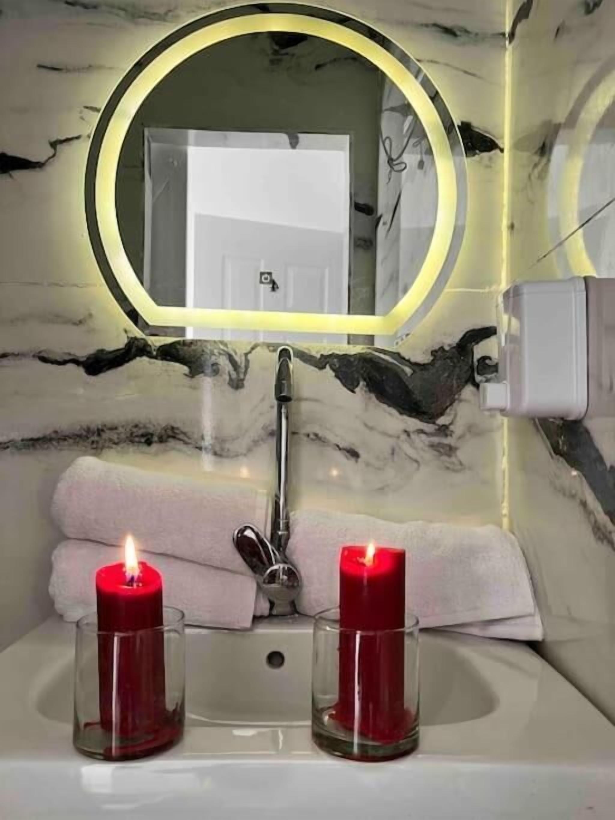 Un baño con lavamanos de mármol, dos velas y un espejo con marco amarillo.