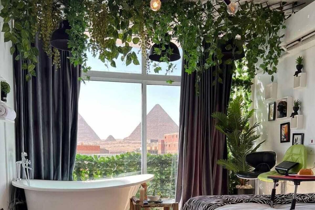Une chambre avec une grande fenêtre, une baignoire, une couvre-lit à motifs zébrés et une vue sur les pyramides.