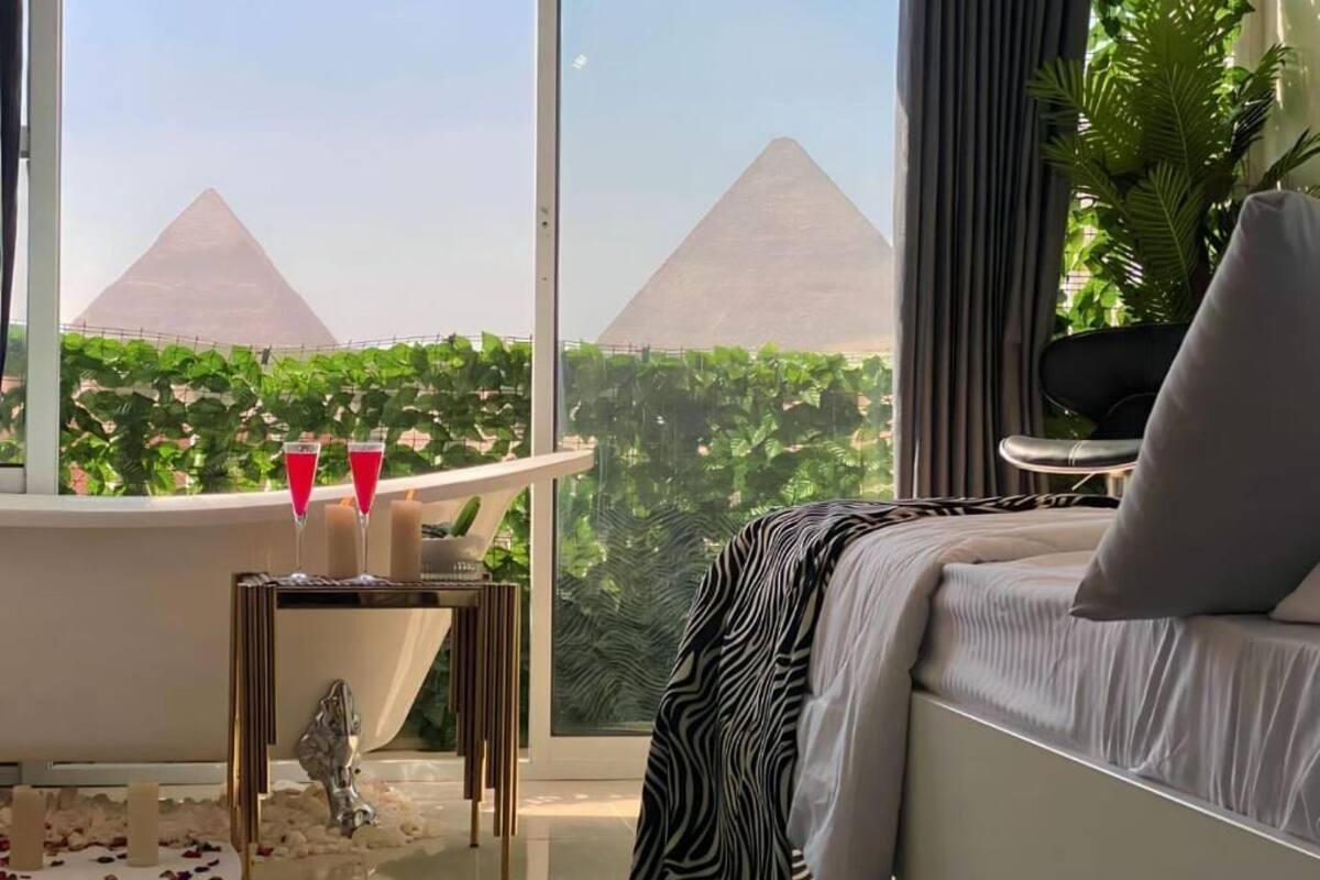 Une chambre moderne avec vue sur les pyramides, une baignoire et une petite table décorée de bougies.