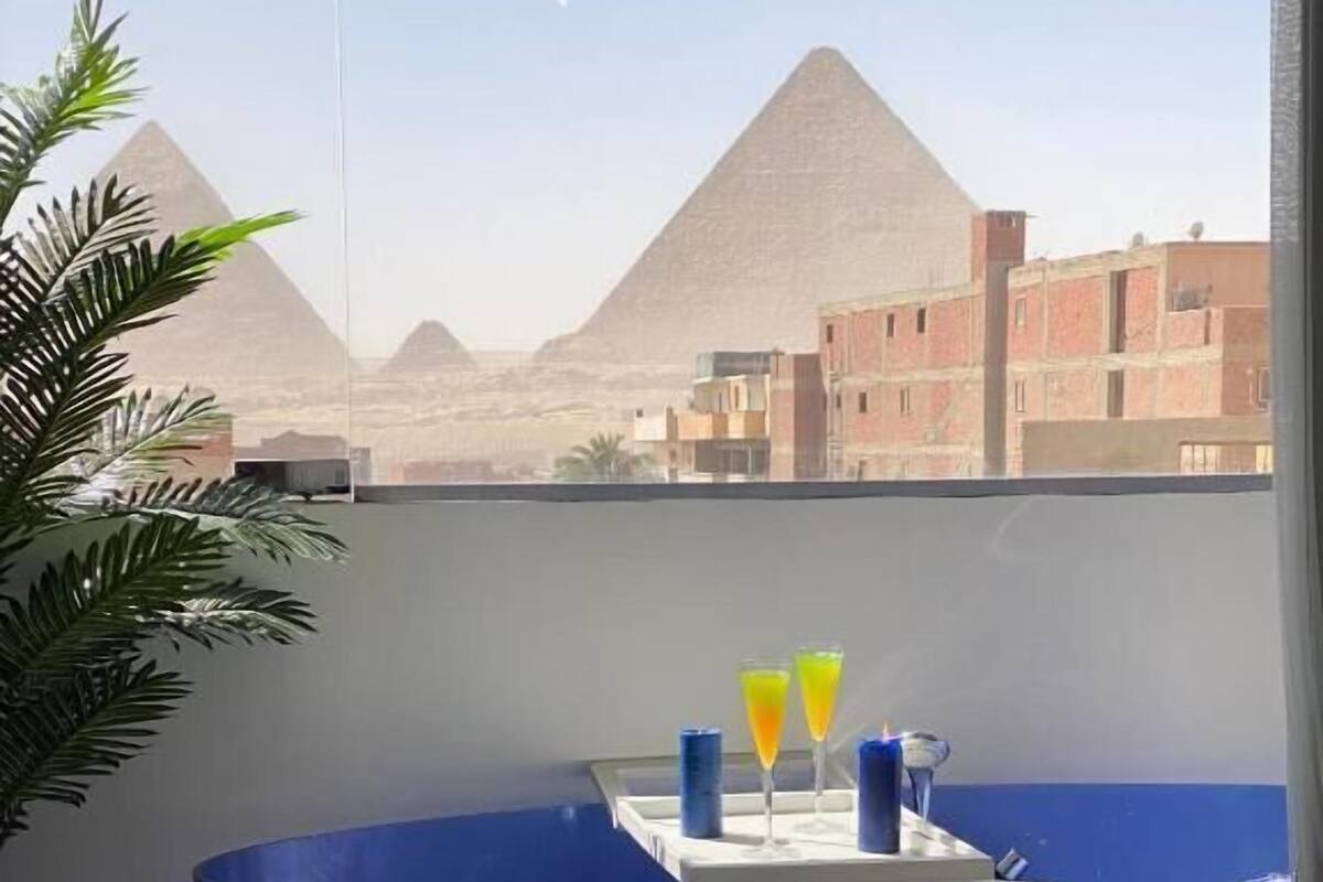 Une salle de bain moderne avec une grande baignoire, un plateau avec deux verres de jus d’orange et, en arrière-plan, une vue sur les pyramides.