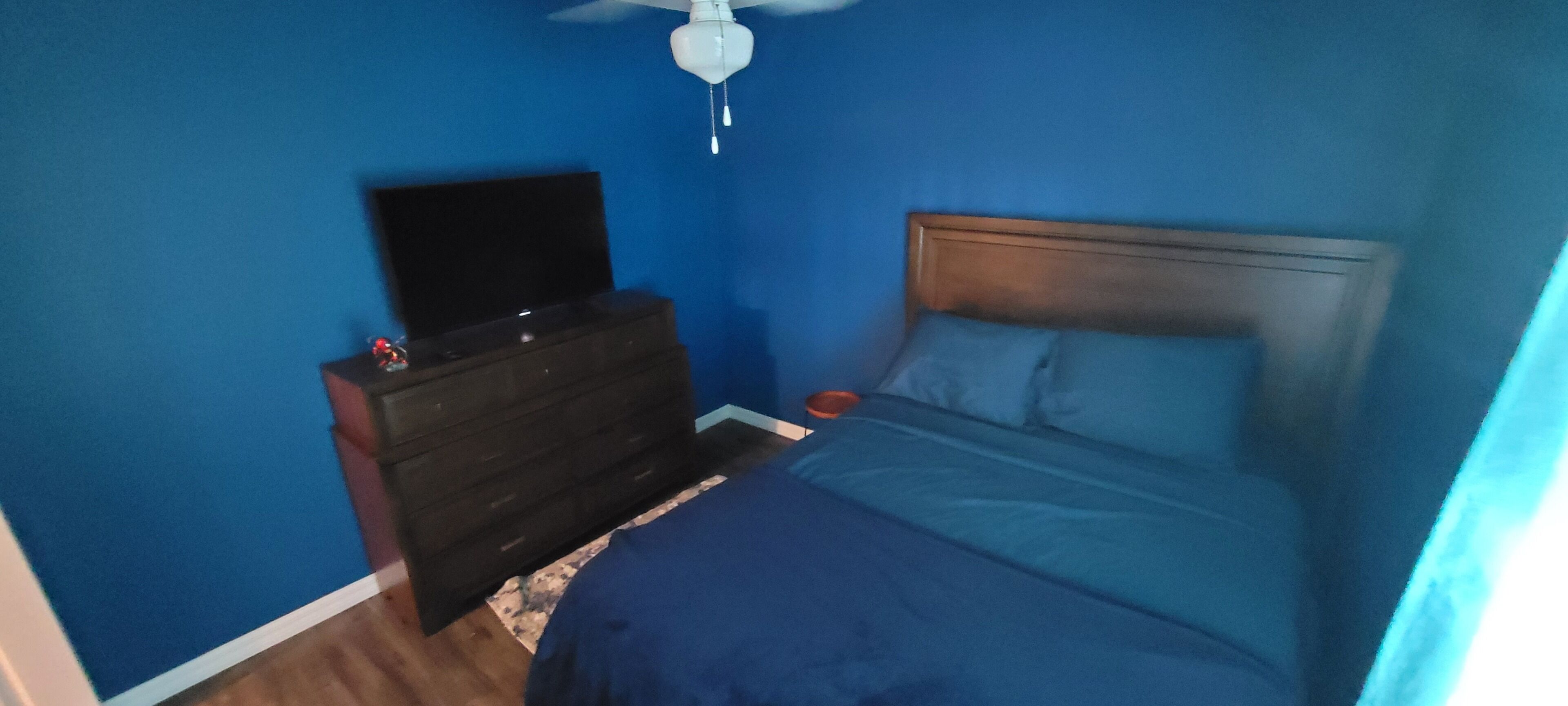A bedroom with a bed, dresser, and a ceiling fan.