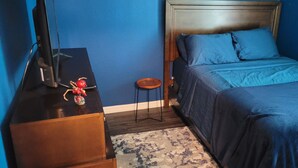 A bedroom with a bed, a wooden dresser, a small stool, and a television on a stand.