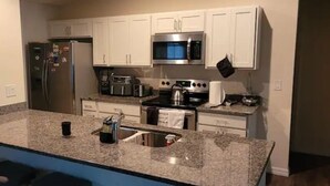 A modern kitchen with white cabinets, a granite countertop, stainless steel appliances, and a built-in oven.