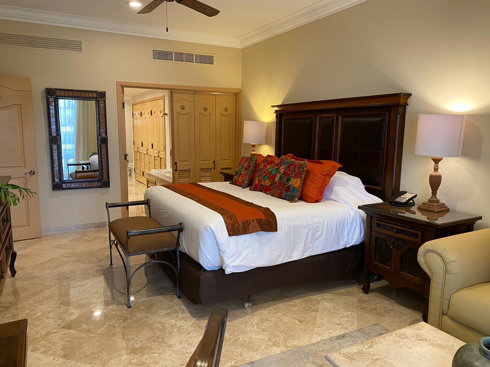 A hotel room with a large bed, a desk, a chair, a mirror, a wardrobe, and a ceiling fan.
