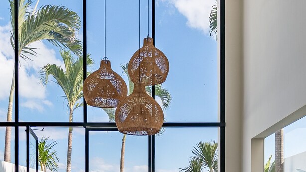 A spacious living area with a large window, a green sofa, wooden chairs, and a small round table. - Villa Vybe (Canggu)