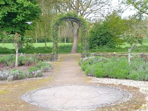 A garden pathway leading to an arched entrance surrounded by lush greenery and a circular stone design.