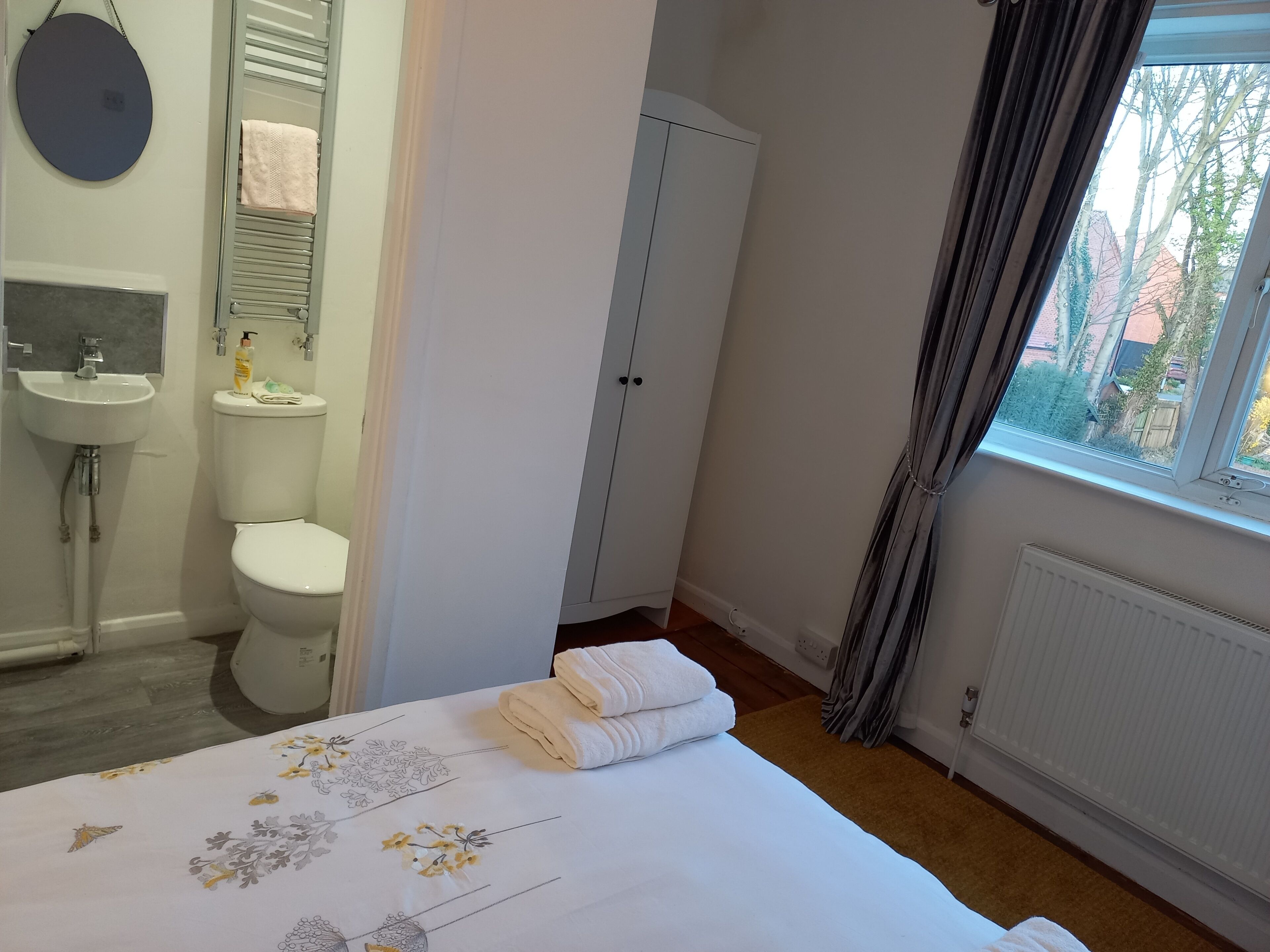 Quarto com cama, janela, radiador, guarda-roupa, banheiro com pia e vaso sanitário, e espelho.