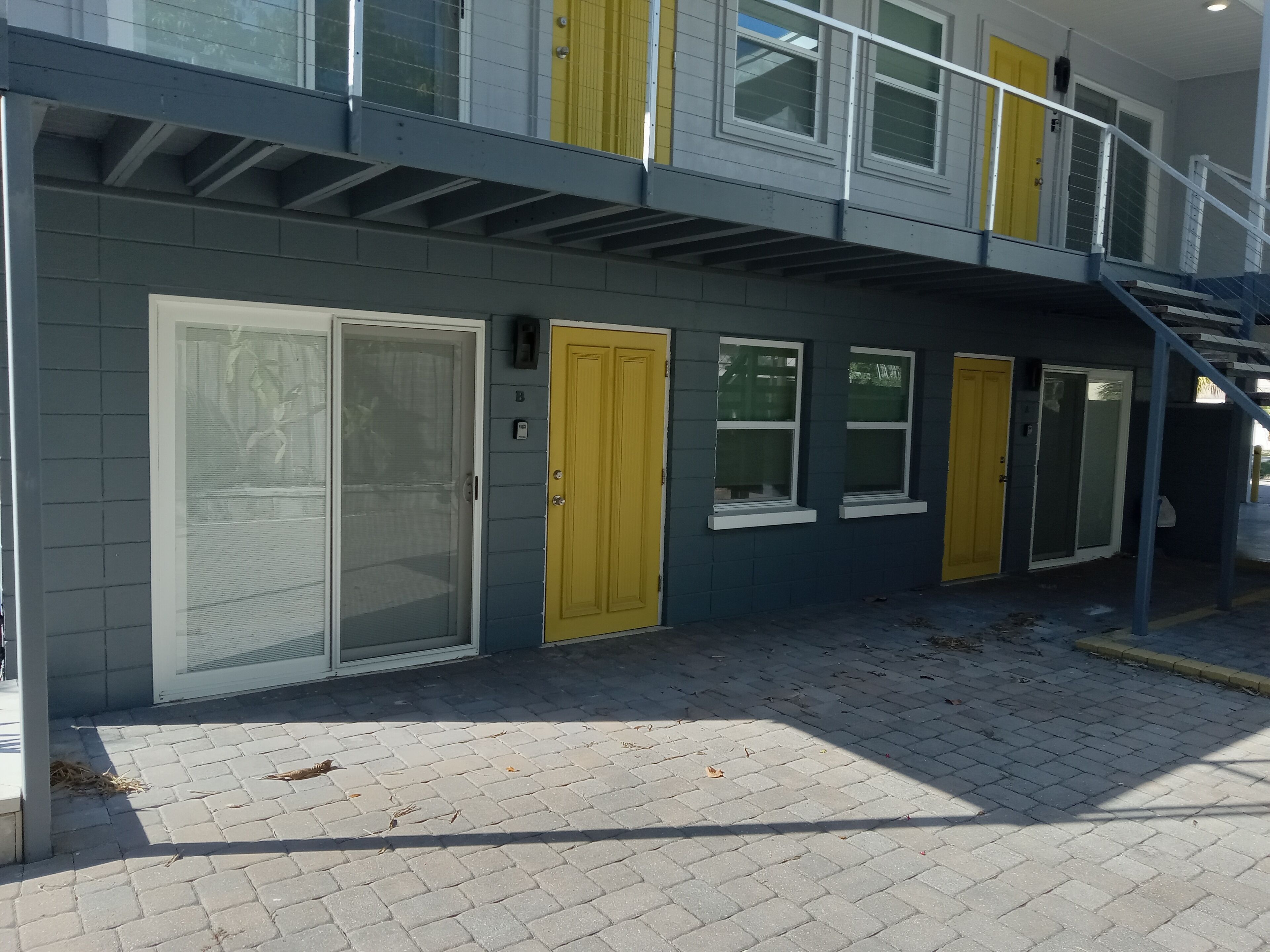Een gebouw met een grijze buitenkant, gele deuren en een overdekt buitengebied met een trap.
