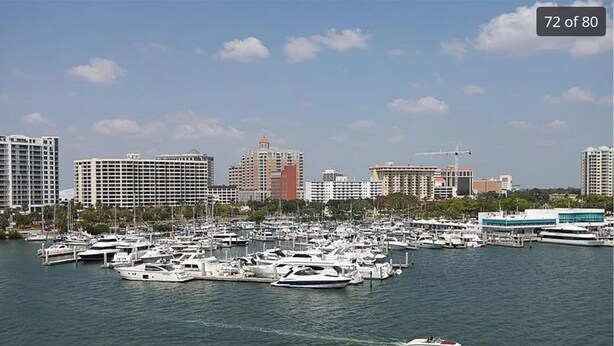 A marina with numerous boats docked, surrounded by high-rise buildings and a clear sky.