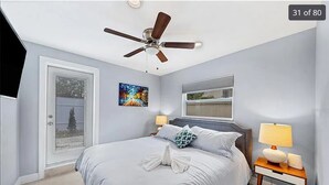 A bedroom with a bed, a ceiling fan, a nightstand with a lamp, and a window.